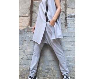 Könnte beinhalten: Ein hellgraues ärmelloses Kapuzentunika mit schwarzem Reißverschluss und passender Hose. Das Outfit wird mit schwarz-weißen High-Top-Sneakern kombiniert. Das Model steht vor einer verwitterten Backsteinmauer.