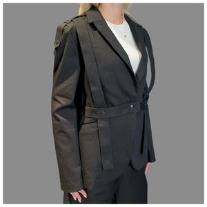 Back view of black avant-garde blazer with tailored fit, asymmetric strap design, and structured silhouette.