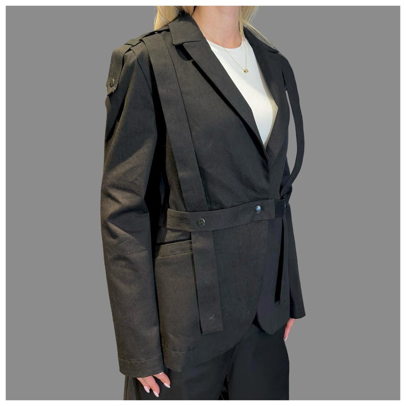 Back view of black avant-garde blazer with tailored fit, asymmetric strap design, and structured silhouette.