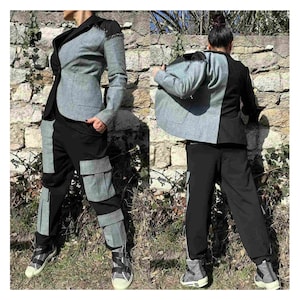 May include: A two-toned blazer with one side black and the other side a light grey denim. The blazer is paired with black trousers that have grey denim panels.