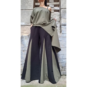 Può includere: Un top asimmetrico verde oliva con una sola spallina e maniche lunghe. L'outfit comprende pantaloni neri a gamba larga con pannelli verde oliva. L'abbigliamento è realizzato in un tessuto morbido e fluido.