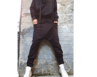 May include: A black long-sleeve hooded sweatshirt with a front kangaroo pocket and matching black drop-crotch pants featuring side pockets. The outfit is paired with white high-top sneakers, creating a monochromatic look with a relaxed fit.