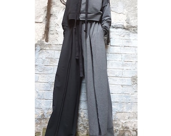 May include: A two-tone outfit featuring a hooded sweatshirt and wide-leg pants. The top is split, with one side black and the other gray. The pants mirror this design, creating a striking visual contrast. The outfit is made of a soft material.