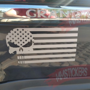 Könnte beinhalten: Ein schwarz-weißes amerikanisches Flaggen-Aufkleber mit einem Totenkopf in der oberen linken Ecke. Der Aufkleber befindet sich auf einem schwarzen Auto mit dem Wort "GRAND CHEROKEE" auf der Rückseite.