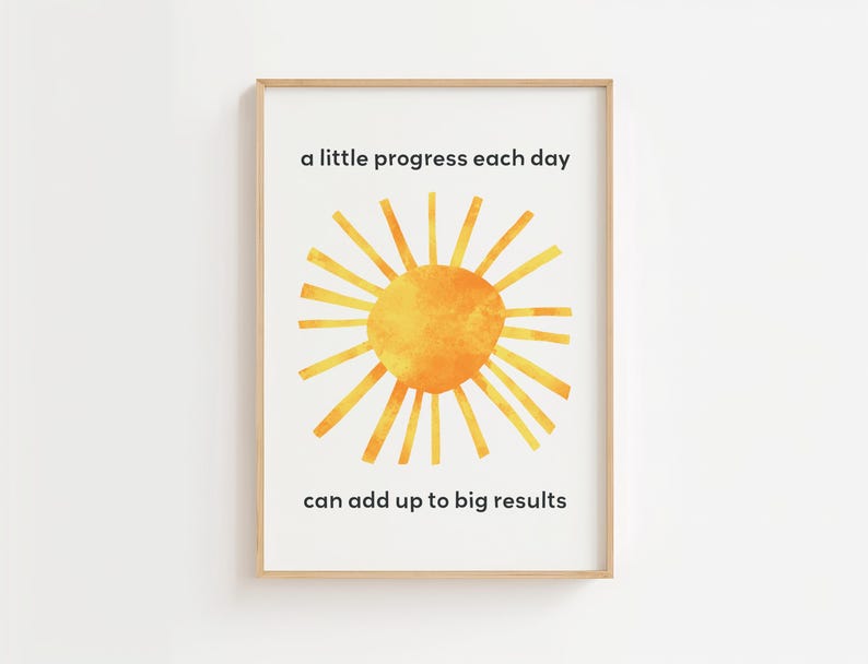 May include: Framed art print with a watercolor sun design in shades of yellow and orange. The print includes the text "a little progress each day can add up to big results" in a simple black font.