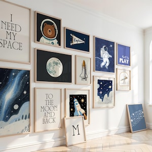 Może przedstawiać: Kolekcja oprawionych wydruk&oacute;w artystycznych o tematyce kosmicznej. Wydruki przedstawiają ilustracje niedźwiedzia astronauty, księżyca, rakiety oraz teksty "I NEED MY SPACE", "TO THE MOON AND BACK" i "let's PLAY". Paleta kolor&oacute;w obejmuje odcienie niebieskiego, białego i brązowego.