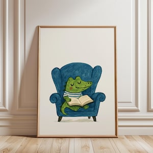 Könnte beinhalten: Gerahmter Kunstdruck mit einer Illustration eines grünen Alligators, der in einem blauen Sessel ein Buch liest. Der Alligator trägt ein gestreiftes Hemd. Das Kunstwerk ist vor einem weißen Hintergrund platziert.