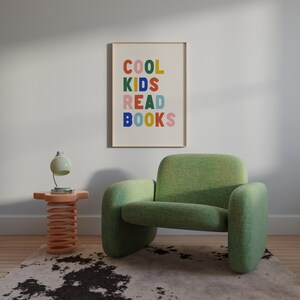 May include: A green armchair with a colorful framed print that reads "COOL KIDS READ BOOKS" hanging on the wall behind it. A small wooden side table with a spring base sits in front of the chair.