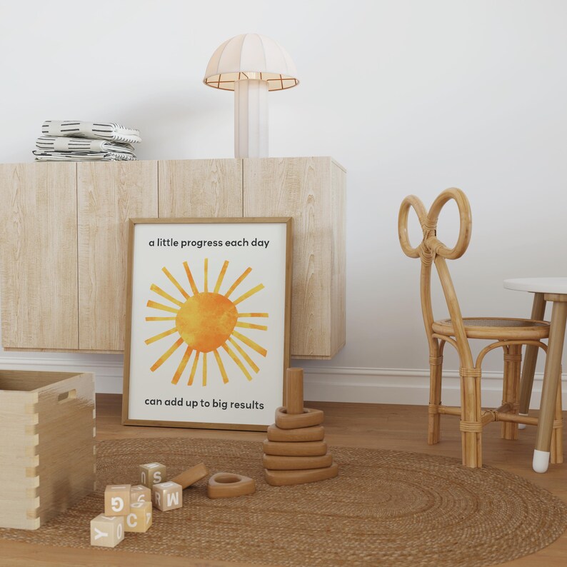 A sun inspired by Eric Carle's collage with a motivational quote for kids about growth mindset. The quote states: a little progress each day can add up to big results. A single frame on the floor is shown in a kids room.