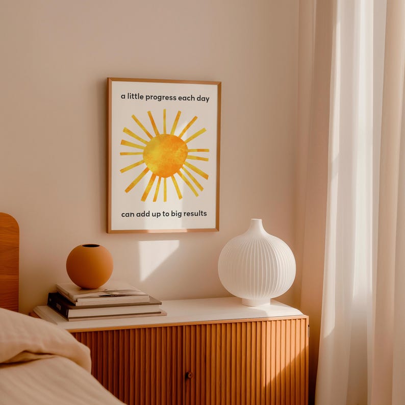 A sun inspired by Eric Carle's collage with a motivational quote for kids about growth mindset. The quote states: a little progress each day can add up to big results. A single frame is shown hanging in a bedroom.