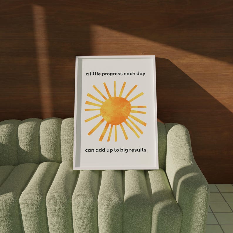A sun inspired by Eric Carle's collage with a motivational quote for kids about growth mindset. The quote states: a little progress each day can add up to big results. A single frame is shown resting on a green sofa.