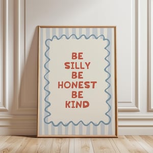 Puede incluir: Un cuadro enmarcado con las palabras "BE SILLY BE HONEST BE KIND" en rojo sobre un fondo crema con rayas verticales azules. La impresi&oacute;n est&aacute; enmarcada en un marco marr&oacute;n claro con un borde azul ondulado. Decoraci&oacute;n de pared.
