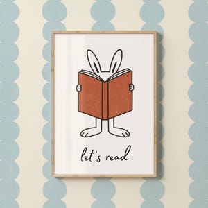 Könnte beinhalten: Gerahmte Illustration mit einem Cartoon-Hasen, der ein Buch mit braunem Einband liest. Die Ohren und Füße des Hasen sind sichtbar, und der Text "let's read" steht darunter. Der Hintergrund ist ein hellblaues und weißes Muster.