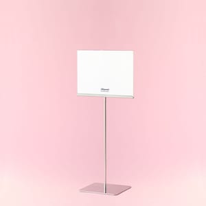 Op de afbeelding: Een zilveren metalen bordenhouder met een vierkante basis en een lange, dunne paal die een wit rechthoekig bord ondersteunt. Op het bord staat de tekst "Altarmi". De achtergrond is effen roze.
