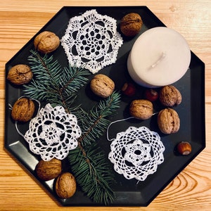 Puede incluir: Una bandeja negra con una variedad de artículos, incluyendo una vela blanca, nueces y doilies de ganchillo. La bandeja está sobre una superficie de madera.