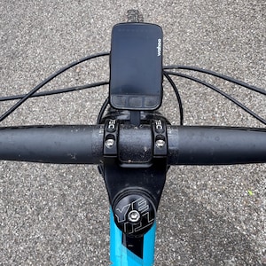 Könnte beinhalten: Ein schwarzer Wahoo Fahrradcomputer, der an einem schwarzen Lenker mit einem schwarzen Vorbau und einem blau-schwarzen Rahmen montiert ist.