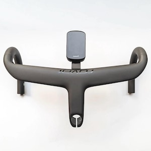 Può includere: Un manubrio per bicicletta grigio scuro con il marchio "ROVAL" stampato sopra. Un dispositivo Garmin nero è montato al centro. Il manubrio ha un design aerodinamico unico.