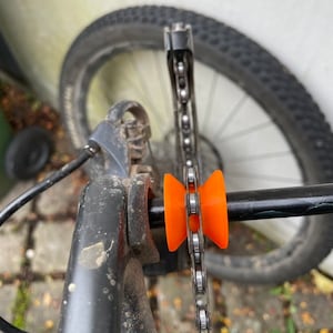 Op de afbeelding: Close-up van een fietsketting met een oranje kettinggeleider. De kettinggeleider is bevestigd aan het fietsframe en helpt voorkomen dat de ketting eraf valt.
