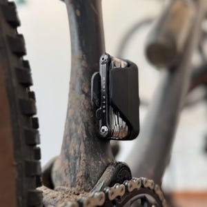 Könnte beinhalten: Ein schwarzes Multi-Tool-Kit mit der Aufschrift "MINI PT 30" ist an einem Fahrradrahmen montiert. Das Werkzeugset wird in einem schwarzen Halter gehalten und enthält verschiedene silberne Werkzeuge. Der Fahrradrahmen ist mit Schmutz und Dreck bedeckt.