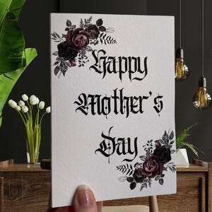 May include: A white card with black gothic lettering that reads "Happy Mother's Day". The card is decorated with black and purple watercolor roses and leaves.