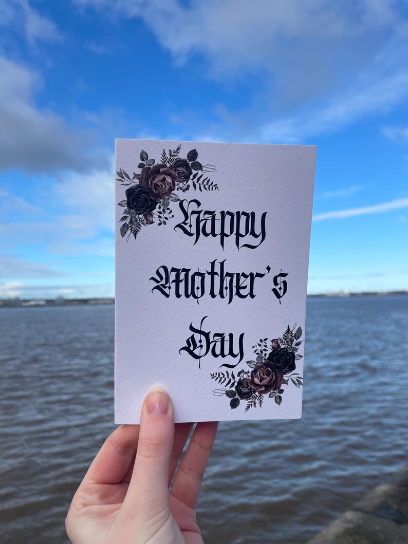 May include: A white card with black gothic lettering that reads "Happy Mother's Day". The card is decorated with black and pink floral illustrations.