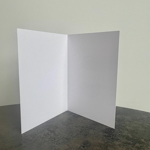 May include: A blank white card with a fold in the middle. The card is sitting on a dark gray surface.
