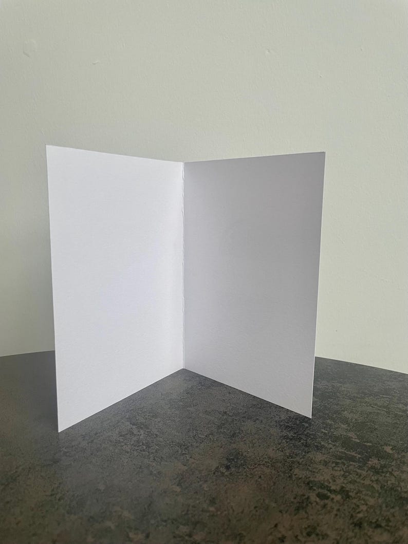 May include: A blank white card with a fold in the middle. The card is sitting on a dark gray surface.