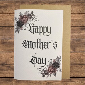 May include: A white card with black gothic lettering that reads "Happy Mother's Day". The card is decorated with a floral design of dark pink and black roses and leaves.