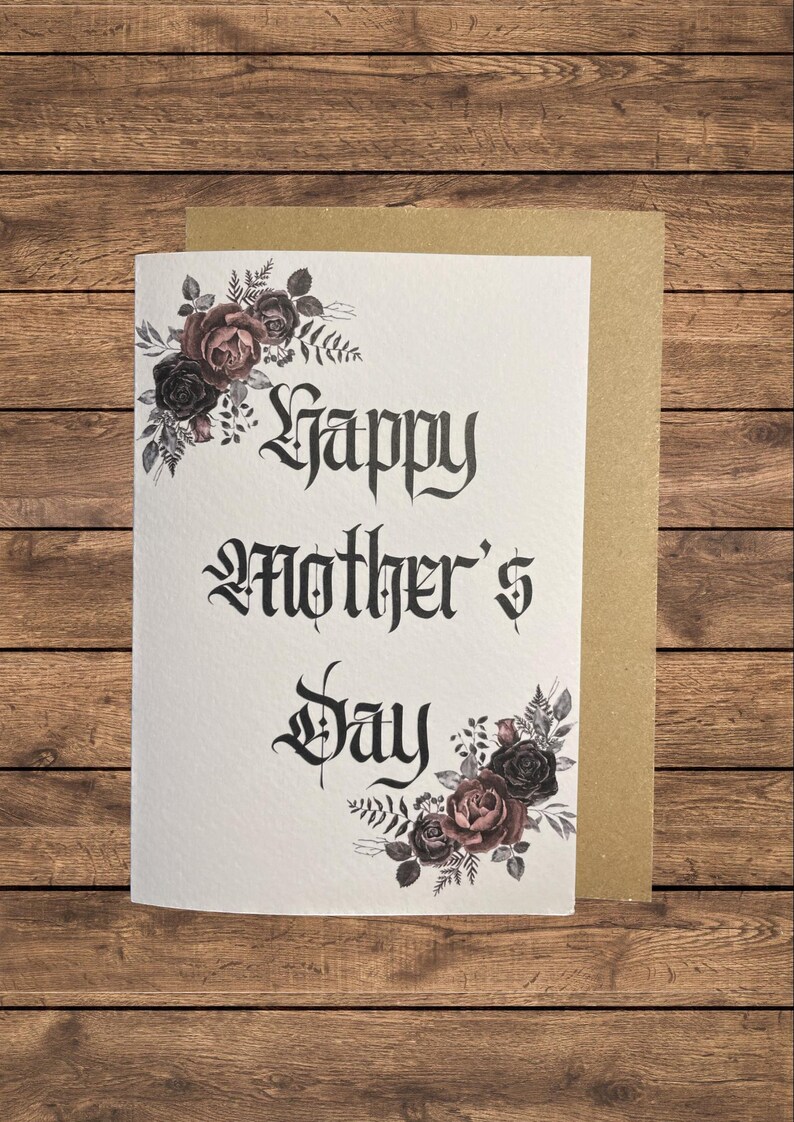 May include: A white card with black gothic lettering that reads "Happy Mother's Day". The card is decorated with a floral design of dark pink and black roses and leaves.