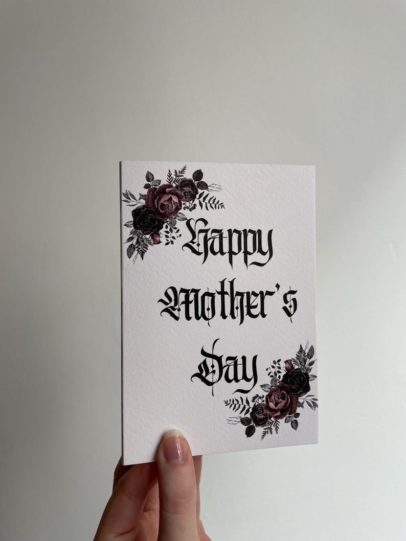 May include: A white card with black gothic lettering that reads "Happy Mother's Day". The card is decorated with black and pink floral illustrations.