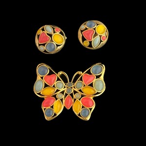 May include: A gold butterfly brooch with red, yellow, and blue enamel accents. The brooch is made of metal and has a detailed design. The butterfly has a pair of matching earrings with the same design.
