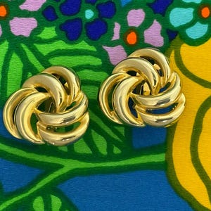 Könnte beinhalten: Ein Paar goldfarbene Ohrclips mit einem gedrehten Knotendesign.