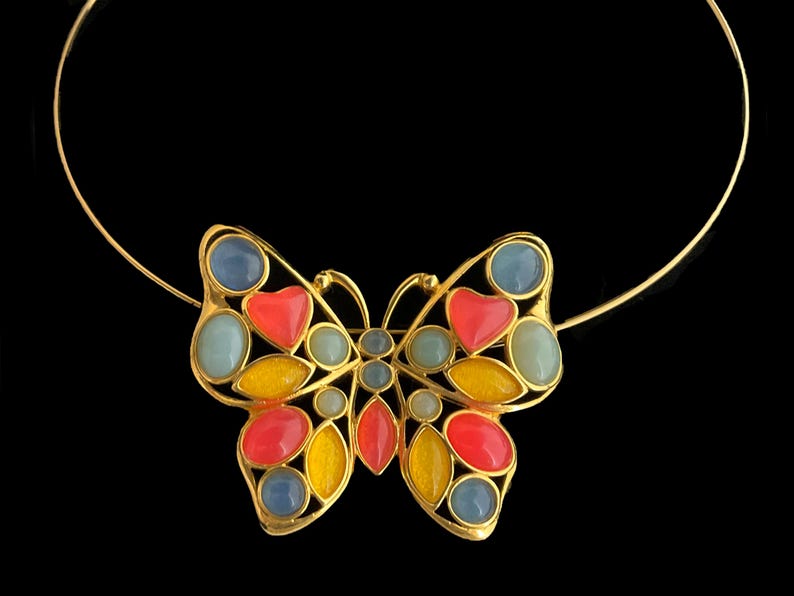 May include: A gold butterfly necklace with colorful stones. The butterfly has blue, red, and yellow stones.