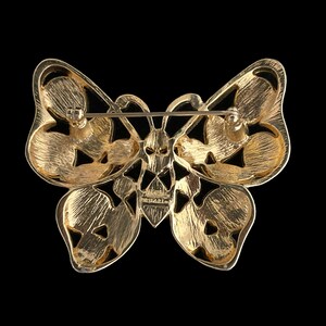 May include: Gold-toned butterfly brooch with intricate cut-out details. The brooch has a pin and catch closure on the back.