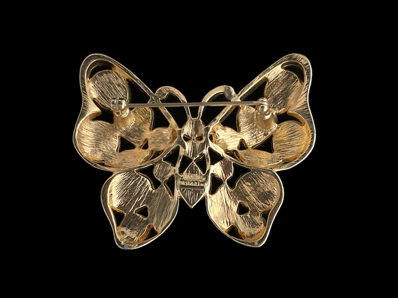 May include: Gold-toned butterfly brooch with intricate cut-out details. The brooch has a pin and catch closure on the back.