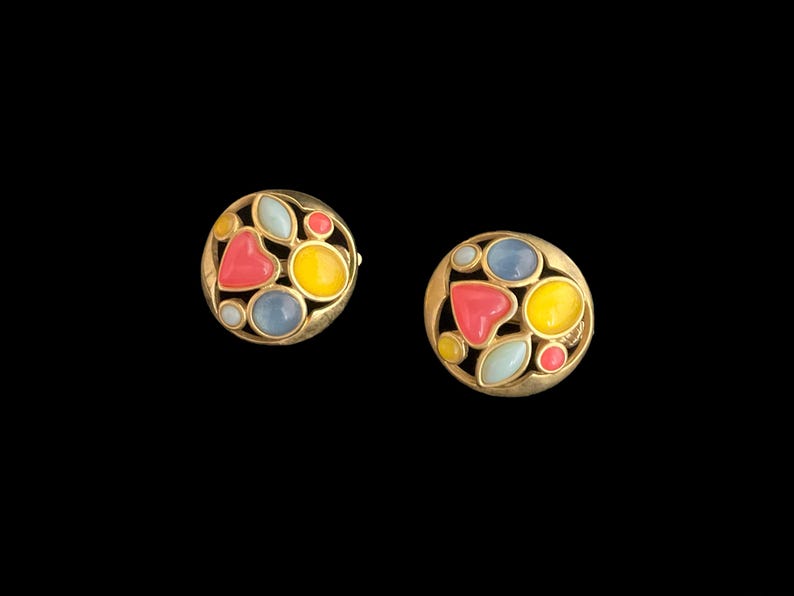 May include: A pair of gold tone earrings with colorful enamel stones in a circular design. The stones are in shades of pink, yellow, blue, and white.