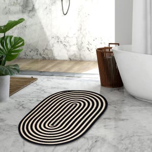 Könnte beinhalten: Ovaler Teppich mit schwarzen und weißen Streifen in modernem Design. Der Teppich ist aus Naturfasern gefertigt und perfekt, um jedem Raum einen Hauch von Stil zu verleihen.