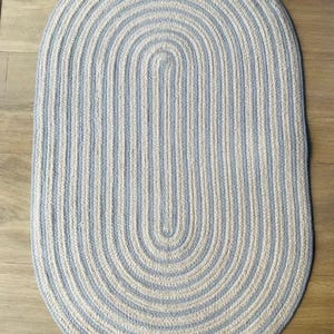 Könnte beinhalten: Ein ovaler geflochtener Teppich in Blau und Weiß mit einem gestreiften Muster. Der Teppich ist aus einem dicken, gewebten Material gefertigt und hat eine weiche, angenehme Textur.