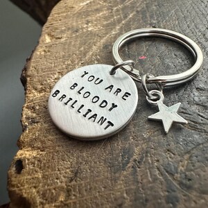 May include: Silver keychain with a round tag that reads "You are bloody brilliant" and a small star charm.
