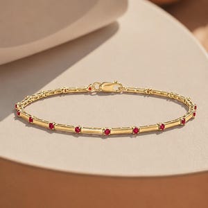 May include: A yellow gold chain bracelet featuring a series of small, round, vibrant red gemstones set at regular intervals along the length of the band. The bracelet includes a secure lobster claw clasp mechanism for fastening the jewelry piece.