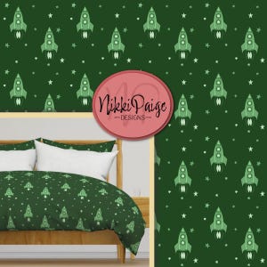 Può includere: Set di biancheria da letto verde con un motivo ripetuto di razzi verdi e stelle bianche su sfondo verde scuro. Il set include un copripiumino e federe. Il marchio "Nikki Paige Designs" è visualizzato su un cerchio rosa.