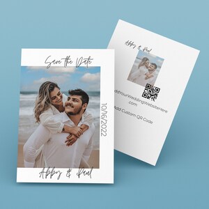May include: Save the date card with a photo of a couple on a beach. The card is white with black text that says "Save the Date" and "Abby & Paul". The date "10/16/2022" is printed on the right side of the card. The back of the card has a smaller photo of the couple and a QR code.