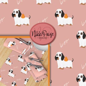 Puede incluir: Manteles individuales, servilletas y platos rosas con un patrón repetido de un perro de dibujos animados con un disfraz de fantasma y una calabaza. La palabra "boo" está escrita en una fuente de script. La marca "Nikki Paige Designs" está en un círculo rosa.