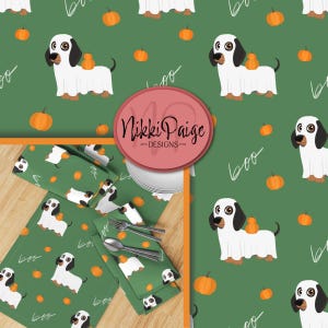 Puede incluir: Patrón verde con temática de Halloween con un diseño repetido de un perro salchicha disfrazado de fantasma, calabazas y la palabra "boo". El patrón se utiliza en servilletas y manteles individuales. La imagen también incluye un logotipo que dice "Nikki Paige - Designs".