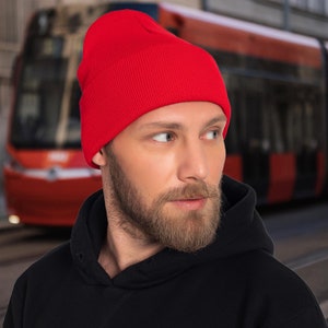 Könnte beinhalten: Eine rote Mütze mit gerippter Struktur. Die Mütze ist aus einem weichen, warmen Material gefertigt und perfekt, um den Kopf im Winter warm zu halten.