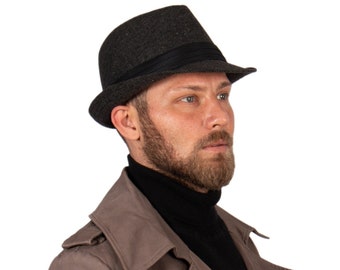 May include: A dark grey fedora hat with a black band. The person is wearing a black turtleneck and a brown trench coat. The coat has a double-breasted design. The image is set against a white background.