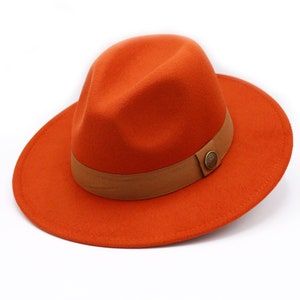 May include: An orange fedora hat with a brown band and a decorative button. The hat has a wide brim and a classic design. The hat is made of a felt-like material.
