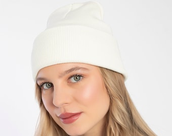Puede incluir: Un gorro de punto blanco con textura de canalé. El gorro lo lleva puesto una persona con el pelo largo y rubio y mira a la cámara.