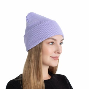 Könnte beinhalten: Eine hellviolette Beanie-Mütze mit gerippter Strickstruktur. Die Mütze ist einfarbig und hat einen umgeschlagenen Saum. Die Mütze wird von einer Person getragen, die ein schwarzes Langarmshirt trägt.