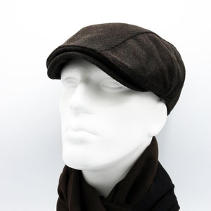 May include: A brown tweed newsboy cap with a slightly curved brim. The cap is on a white mannequin head with a brown scarf.